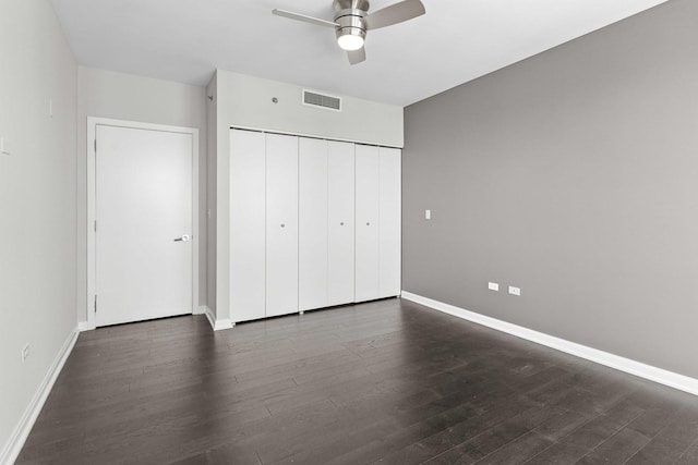 unfurnished bedroom with a closet, visible vents, baseboards, and dark wood finished floors