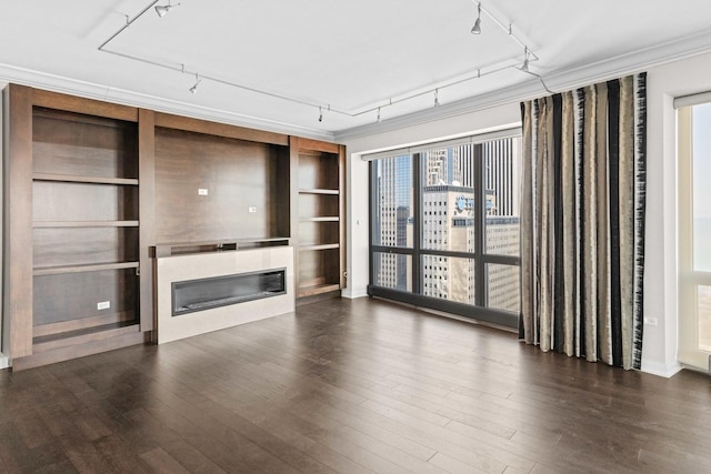 unfurnished living room with dark wood-style flooring, built in features, rail lighting, and a glass covered fireplace