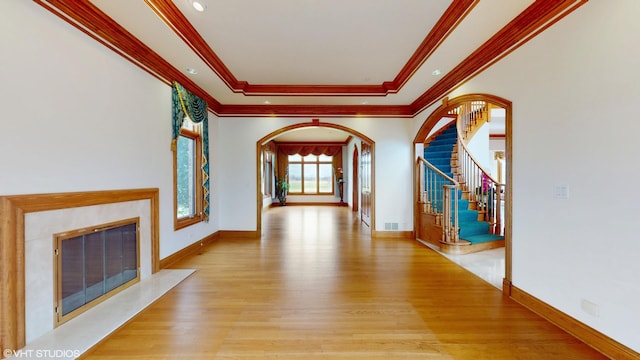 foyer entrance featuring a fireplace, a raised ceiling, light wood-type flooring, stairs, and arched walkways
