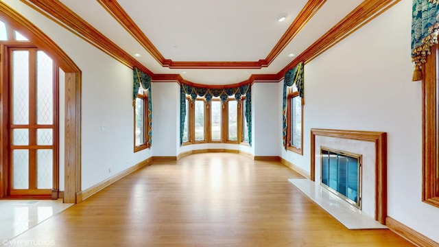 unfurnished living room featuring a tray ceiling, crown molding, light wood-type flooring, baseboards, and a high end fireplace