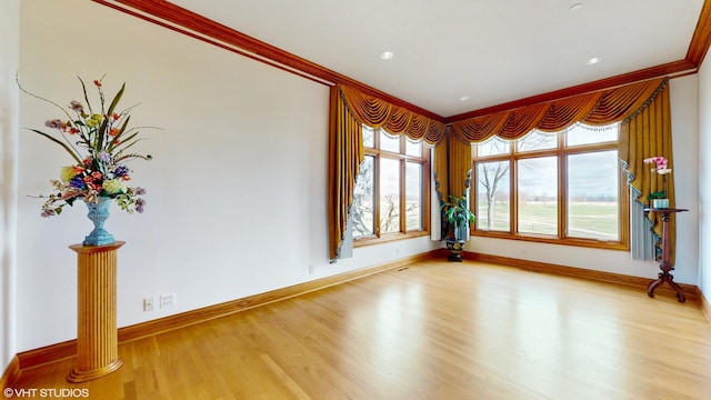 empty room with light wood-style floors, crown molding, and baseboards