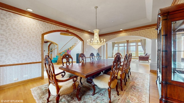 dining space featuring light wood-style flooring, wallpapered walls, arched walkways, an inviting chandelier, and decorative columns