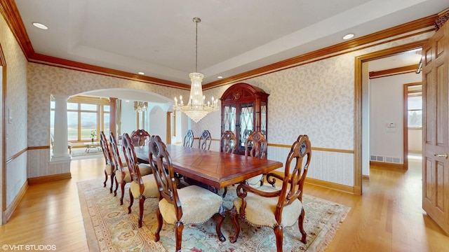 dining room with ornate columns, arched walkways, light wood finished floors, and wallpapered walls