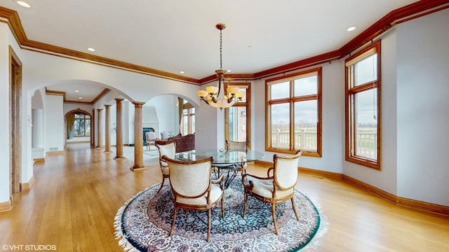 dining space featuring crown molding, light wood-style flooring, baseboards, and arched walkways