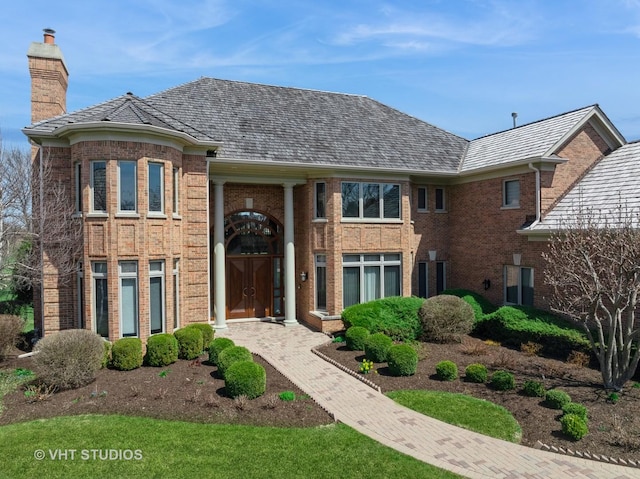 view of front facade featuring brick siding, a high end roof, and a chimney