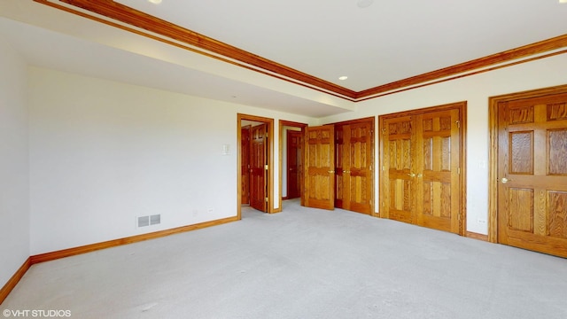 unfurnished bedroom with multiple closets, ornamental molding, carpet flooring, baseboards, and visible vents