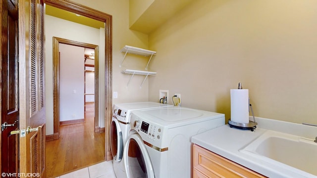 laundry room featuring a sink, washing machine and clothes dryer, cabinet space, and light wood-type flooring