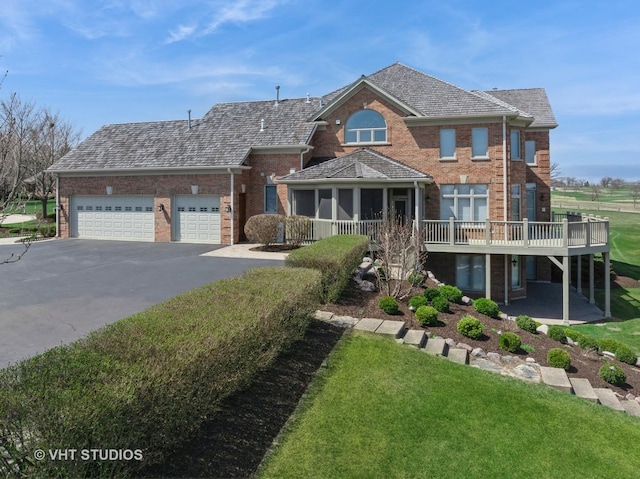 view of front of house with a garage, driveway, a deck, a front yard, and brick siding