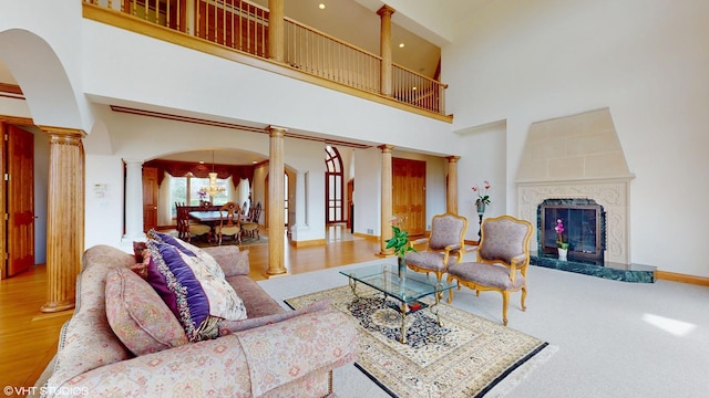 living room with a towering ceiling, arched walkways, a fireplace, ornate columns, and wood finished floors