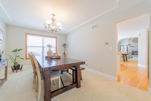 dining room with a chandelier, a brick fireplace, visible vents, and baseboards