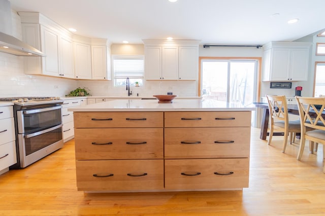 kitchen with light countertops, wall chimney range hood, and range with two ovens