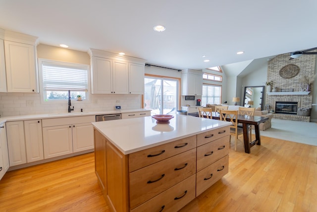 kitchen featuring light countertops, a sink, light wood-style floors, tasteful backsplash, and a brick fireplace