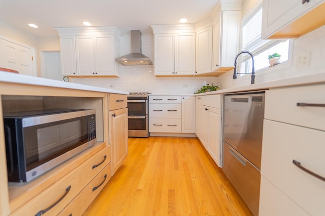 kitchen featuring wall chimney exhaust hood, stainless steel appliances, white cabinetry, decorative backsplash, and light countertops