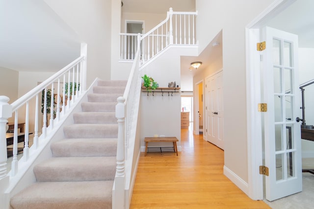 stairway with baseboards, wood finished floors, and a high ceiling