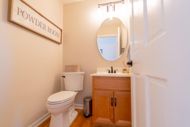 half bath with baseboards, wood finished floors, toilet, and vanity