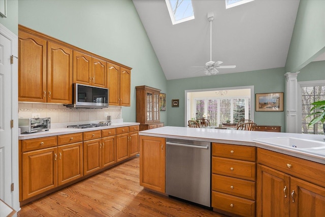 kitchen featuring brown cabinetry, a skylight, appliances with stainless steel finishes, light countertops, and high vaulted ceiling