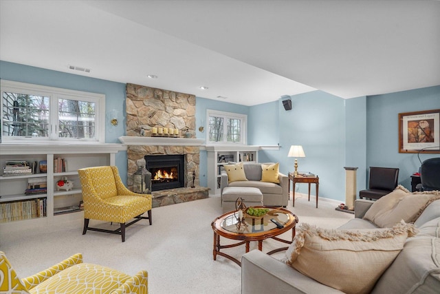 carpeted living room with visible vents, baseboards, a healthy amount of sunlight, and a stone fireplace
