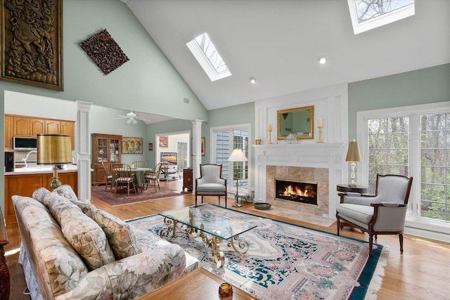 living area with light wood finished floors, a fireplace, high vaulted ceiling, decorative columns, and a skylight