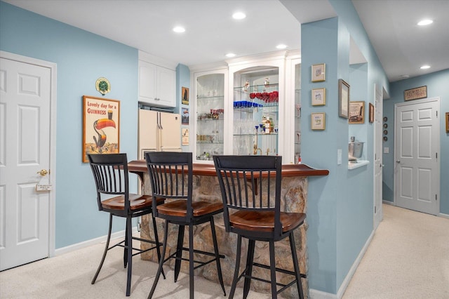 bar with a bar, freestanding refrigerator, baseboards, and light carpet