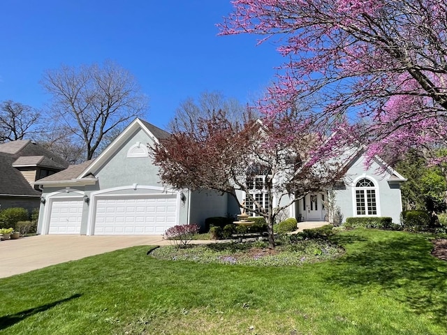 view of front facade featuring a garage, driveway, a front yard, and stucco siding