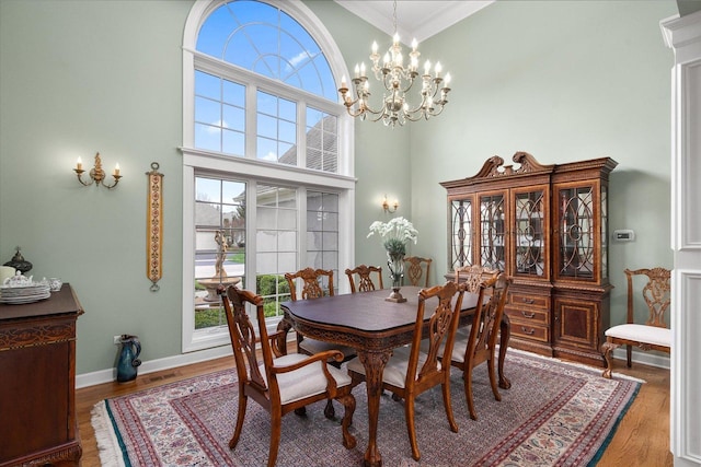dining space with crown molding, a high ceiling, wood finished floors, and a notable chandelier