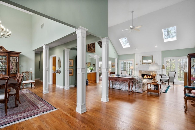 living area with a ceiling fan, a high end fireplace, a skylight, light wood-type flooring, and high vaulted ceiling
