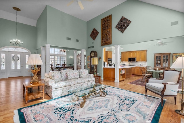 living room featuring ornate columns, high vaulted ceiling, visible vents, and ceiling fan with notable chandelier