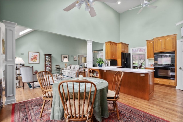 dining room featuring ornate columns, light wood-style floors, ceiling fan, and high vaulted ceiling