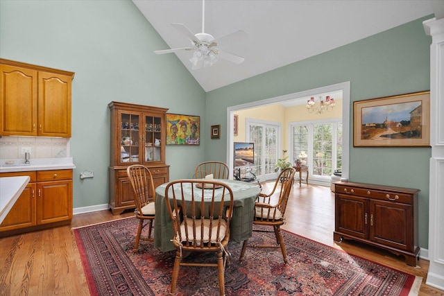 dining room with light wood finished floors, ceiling fan with notable chandelier, and high vaulted ceiling