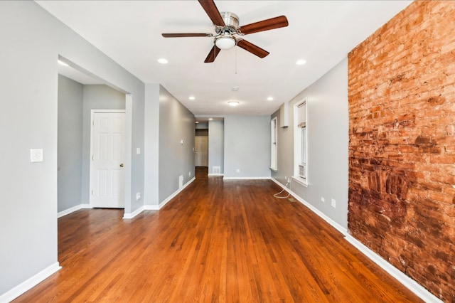 unfurnished room featuring baseboards, wood finished floors, ceiling fan, and brick wall