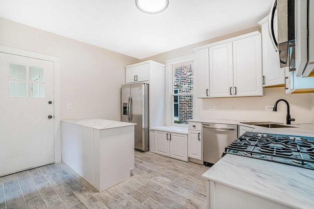 kitchen featuring light stone counters, white cabinetry, a sink, appliances with stainless steel finishes, and light wood-type flooring