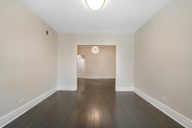 empty room with dark wood-type flooring, visible vents, a chandelier, and baseboards