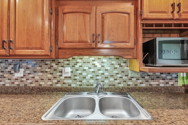 kitchen featuring backsplash, stainless steel microwave, brown cabinets, and a sink