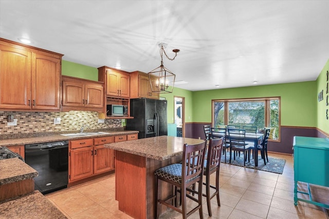kitchen featuring a center island, brown cabinets, a sink, black appliances, and light tile patterned flooring