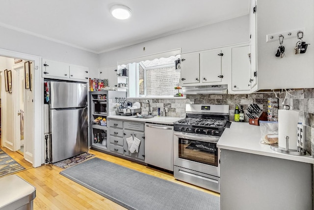 kitchen featuring light countertops, appliances with stainless steel finishes, under cabinet range hood, a sink, and backsplash