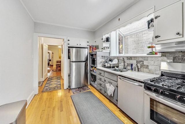 kitchen featuring light countertops, tasteful backsplash, appliances with stainless steel finishes, a sink, and light wood-style floors