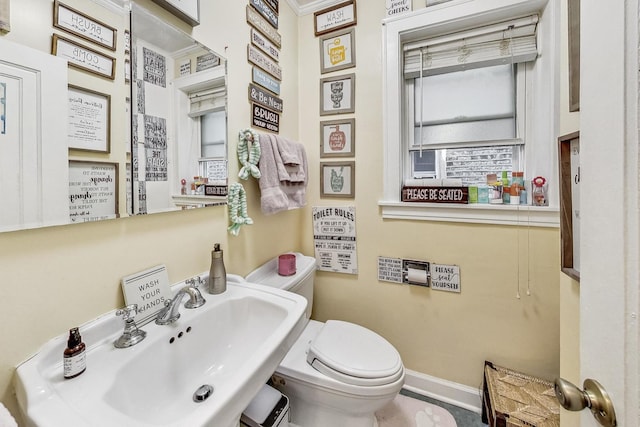 half bath with baseboards, toilet, and a sink