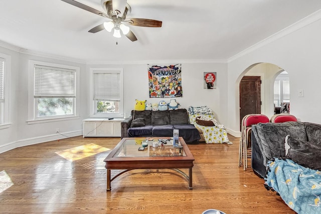 living room featuring ornamental molding, baseboards, arched walkways, ceiling fan, and wood finished floors