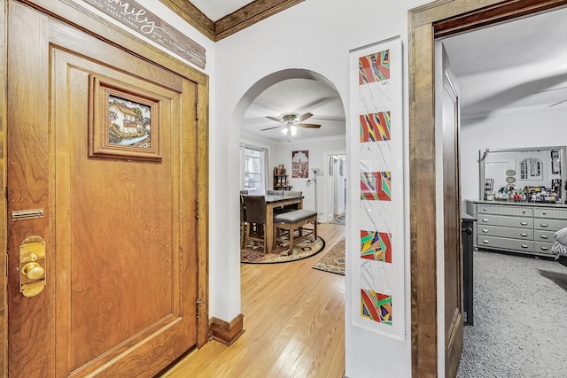 hallway with arched walkways, ornamental molding, and light wood-type flooring