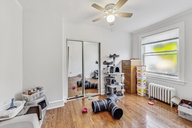 workout room with radiator heating unit, a ceiling fan, baseboards, and wood finished floors
