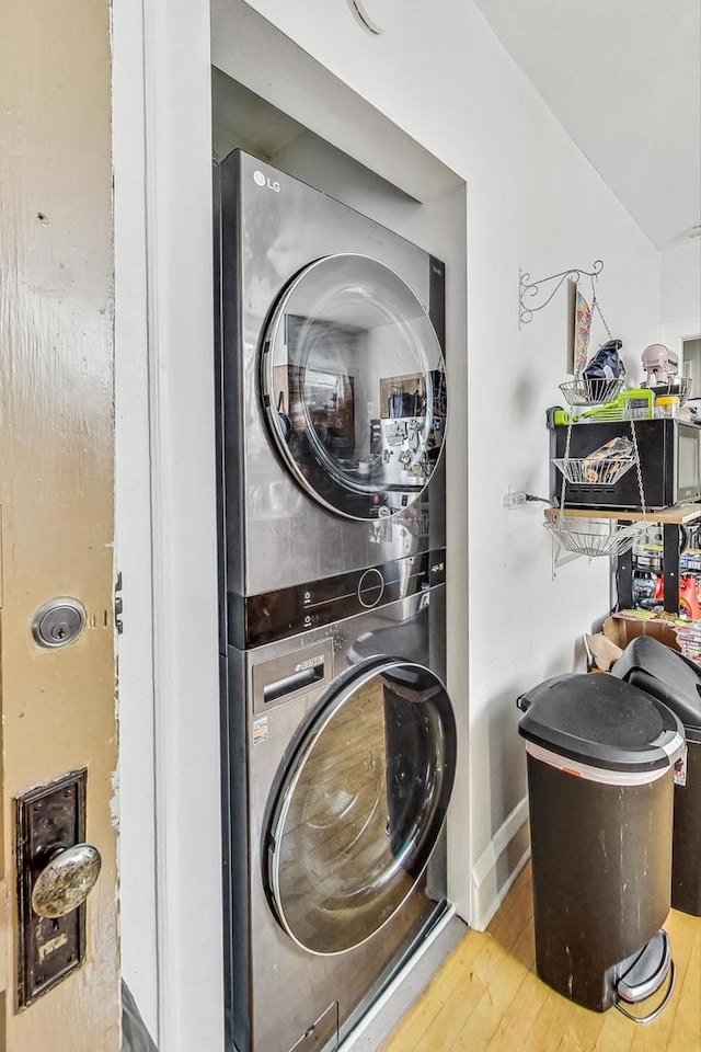 clothes washing area featuring stacked washer and dryer, baseboards, laundry area, and wood finished floors