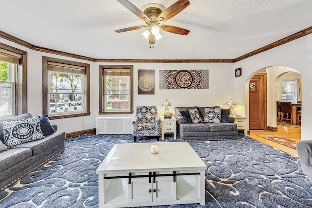 living room with ornamental molding, baseboards, a textured ceiling, arched walkways, and ceiling fan