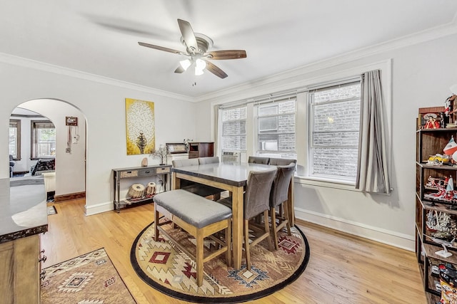 dining area featuring arched walkways, ceiling fan, ornamental molding, and light wood finished floors