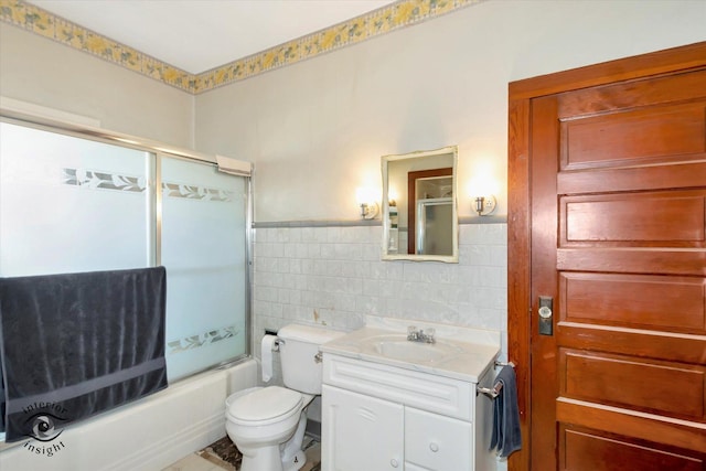 bathroom with toilet, tile walls, vanity, shower / bath combination with glass door, and a wainscoted wall