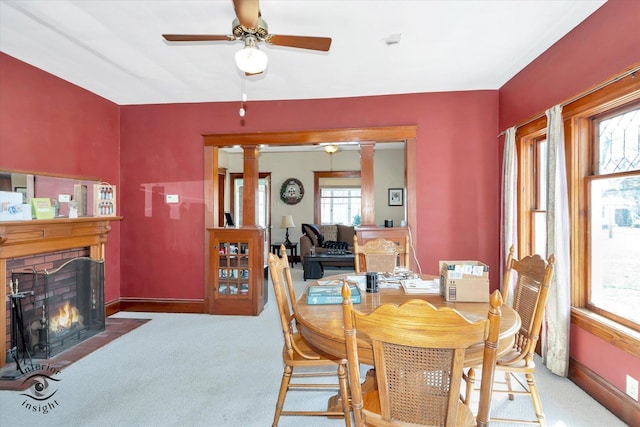 carpeted dining space featuring a fireplace with flush hearth, ornate columns, baseboards, and a ceiling fan