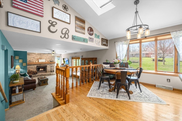 dining room featuring a brick fireplace, wood finished floors, visible vents, and a skylight