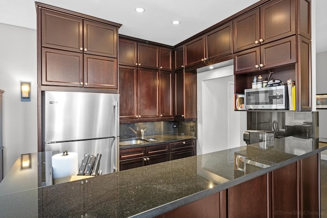 kitchen with decorative backsplash, dark stone countertops, a sink, and stainless steel appliances