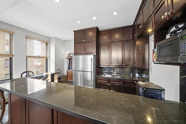 kitchen featuring freestanding refrigerator, a sink, dark stone countertops, and backsplash