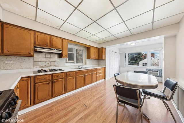 kitchen featuring a sink, light wood-type flooring, brown cabinetry, stove, and under cabinet range hood