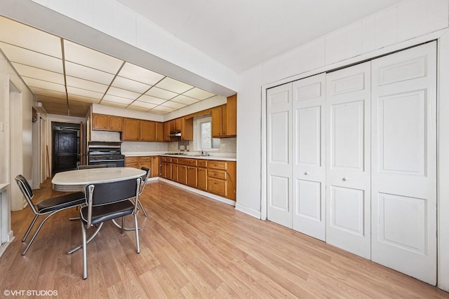 kitchen with light countertops, black range with gas cooktop, backsplash, light wood-style flooring, and brown cabinetry